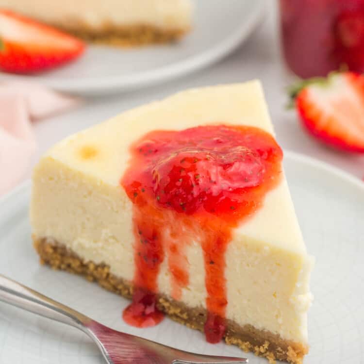 a slice of NY style cheesecake on a small white plate. It's topped with a dollop of strawberry sauce.