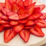 a whole, round, no-bake cheesecake topped with sliced strawberries in a flower pattern