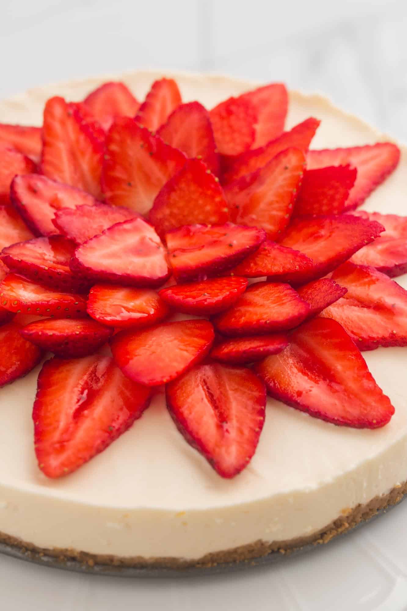 a whole, round, no-bake cheesecake topped with sliced strawberries in a flower pattern