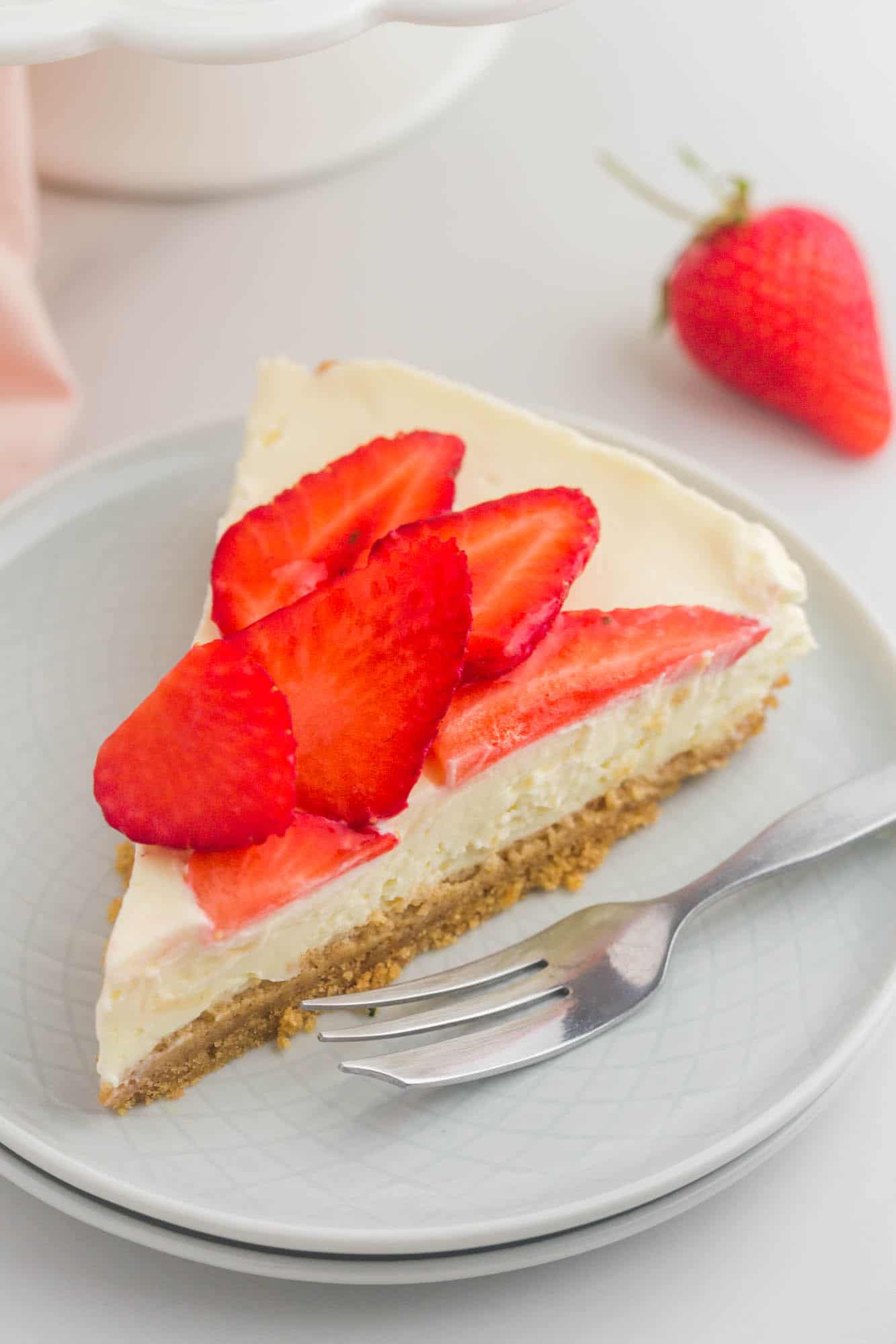 a slice of no bake cheesecake topped with sliced strawberries on a dessert plate with a silver fork