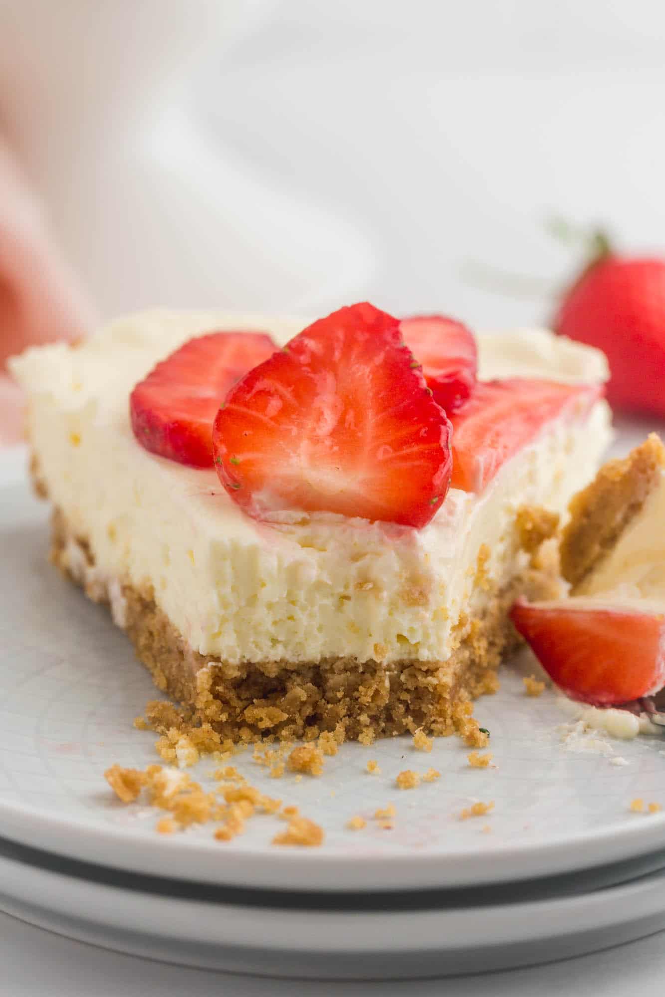 a slice of no bake cheesecake topped with strawberries. A bite has been taken from the front of the slice.