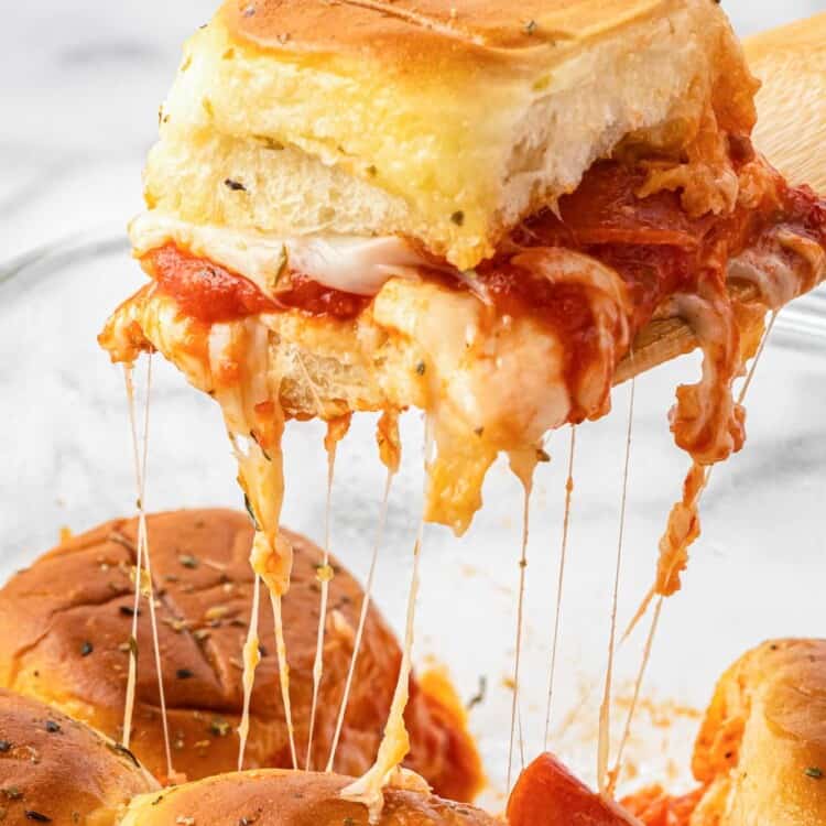 a pizza slider on a Hawaiian roll being lifted out of the pan, mozzarella cheese strings hang down.
