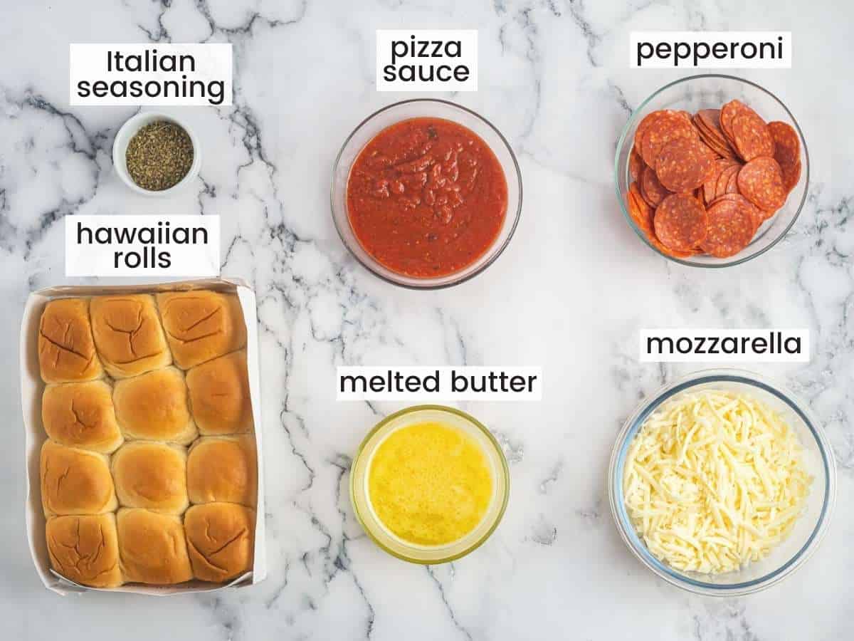 The ingredients for making pizza sliders: cheese, sauce, pepperoni, butter, seasonings, and hawaiian rolls, on a counter, viewed from above