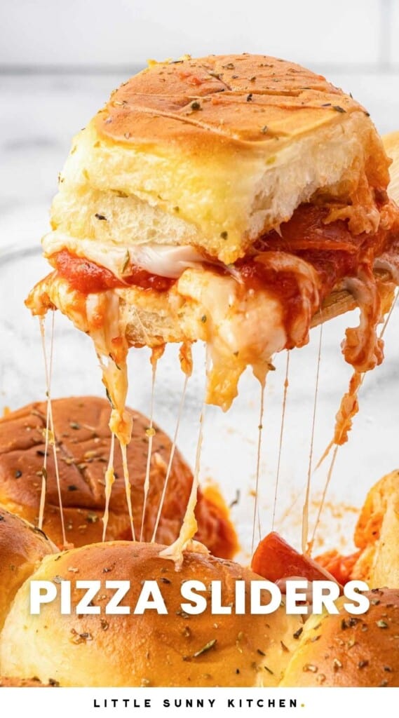 a pizza slider on a Hawaiian roll being lifted out of the pan, mozzarella cheese strings hang down.
