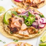 Three salmon tacos with toppings on a cutting board, open-faced.