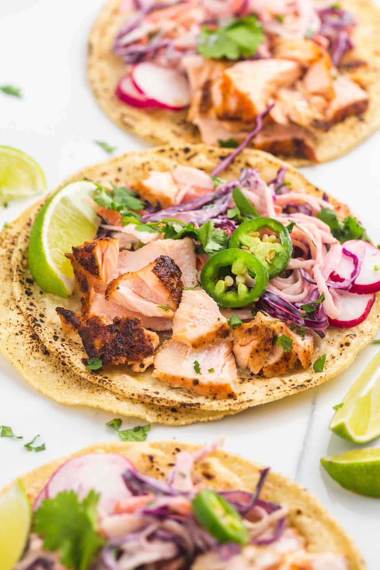 Three salmon tacos with toppings on a cutting board, open-faced.