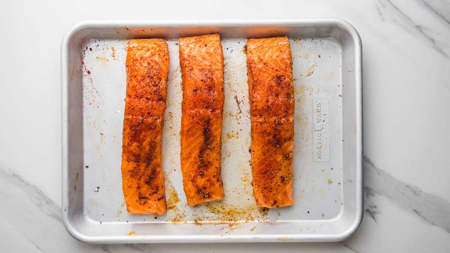 raw salmon fillets with seasoning on a sheet pan. 