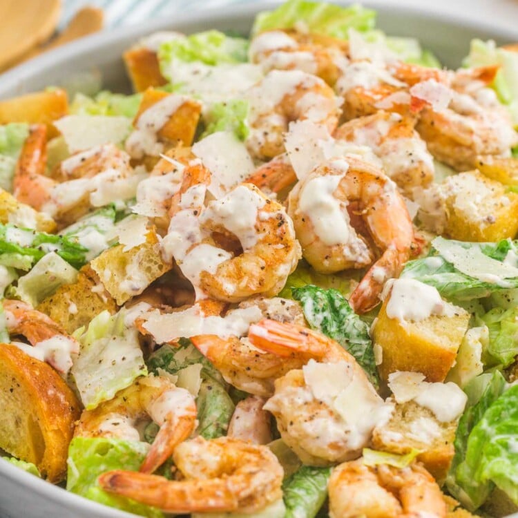 a large white bowl filled with caesar salad topped with shrimp