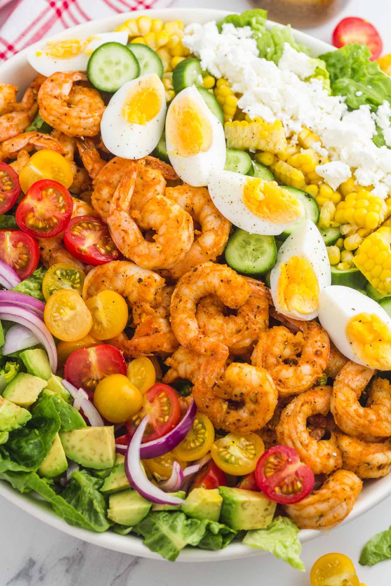 a large shrimp cobb salad with rows of shrimp, eggs, veggies, and blue cheese on top