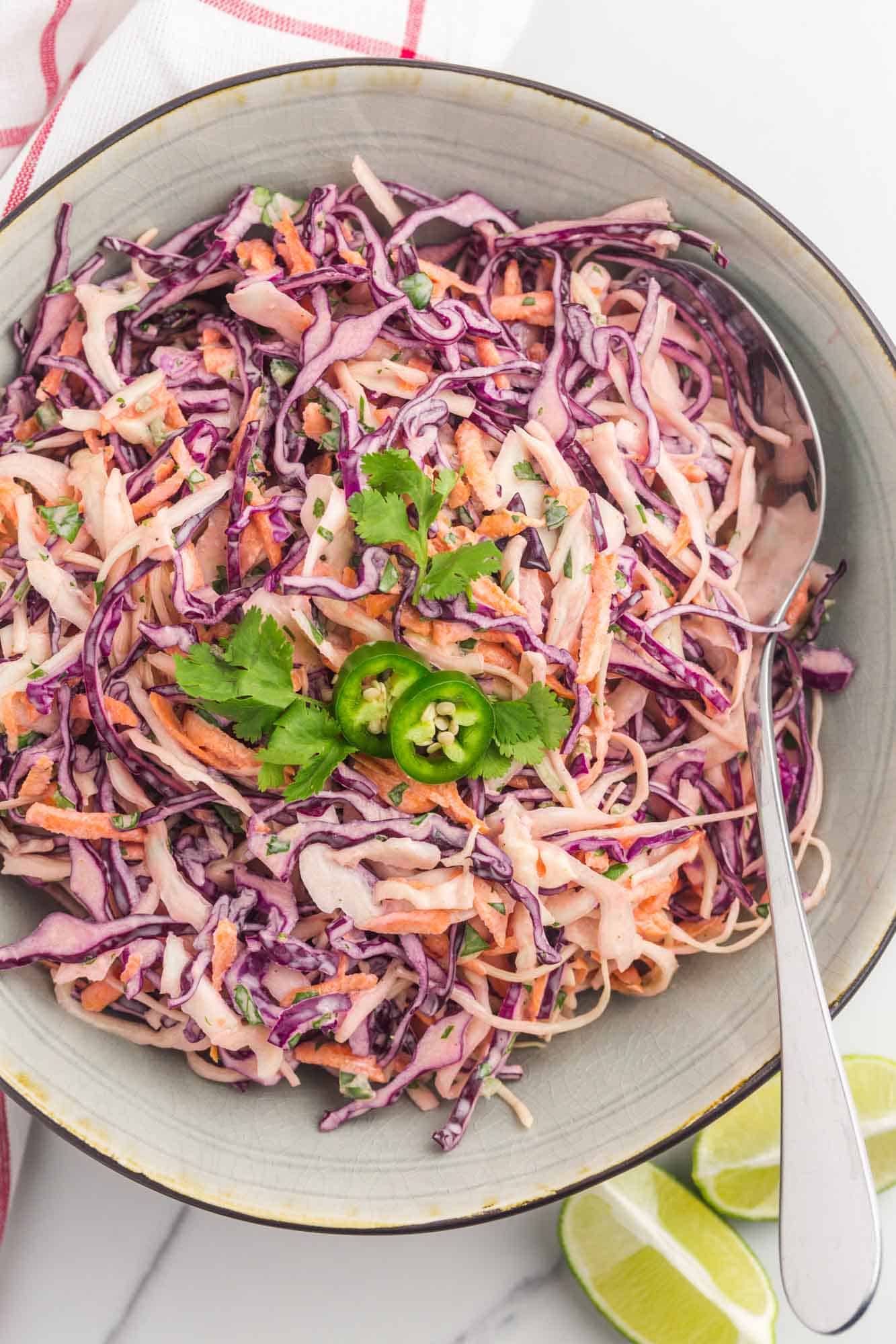 a white bowl filled with creamy cabbage slaw garnished with jalapeno slices and cilantro leaves
