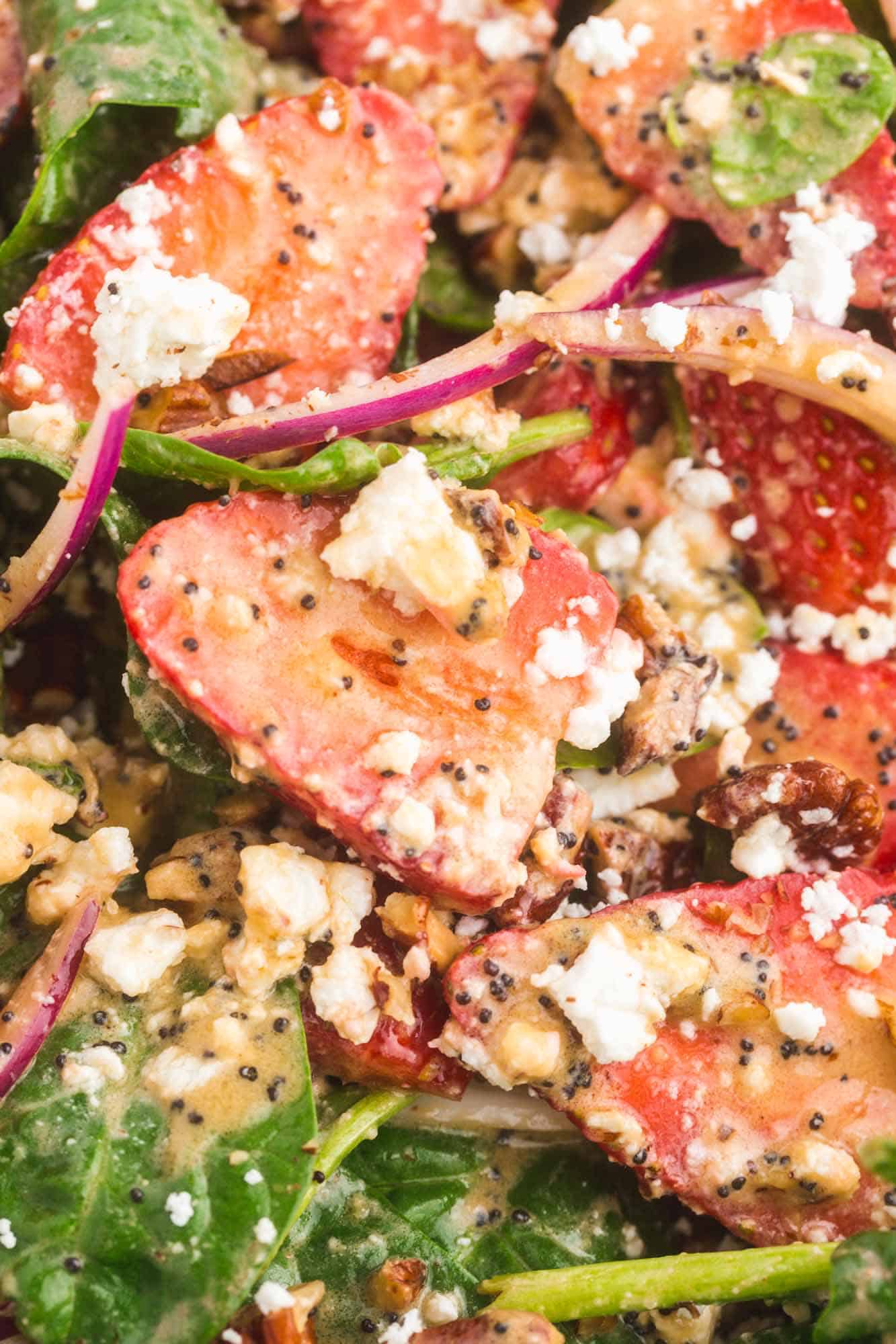 closeup view of a spinach salad with strawberries and poppyseed dressing, feta cheese