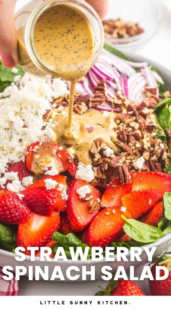 A bowl of spinach salad topped with strawberries, nuts, and cheese. Balsamic dressing is being poured on top