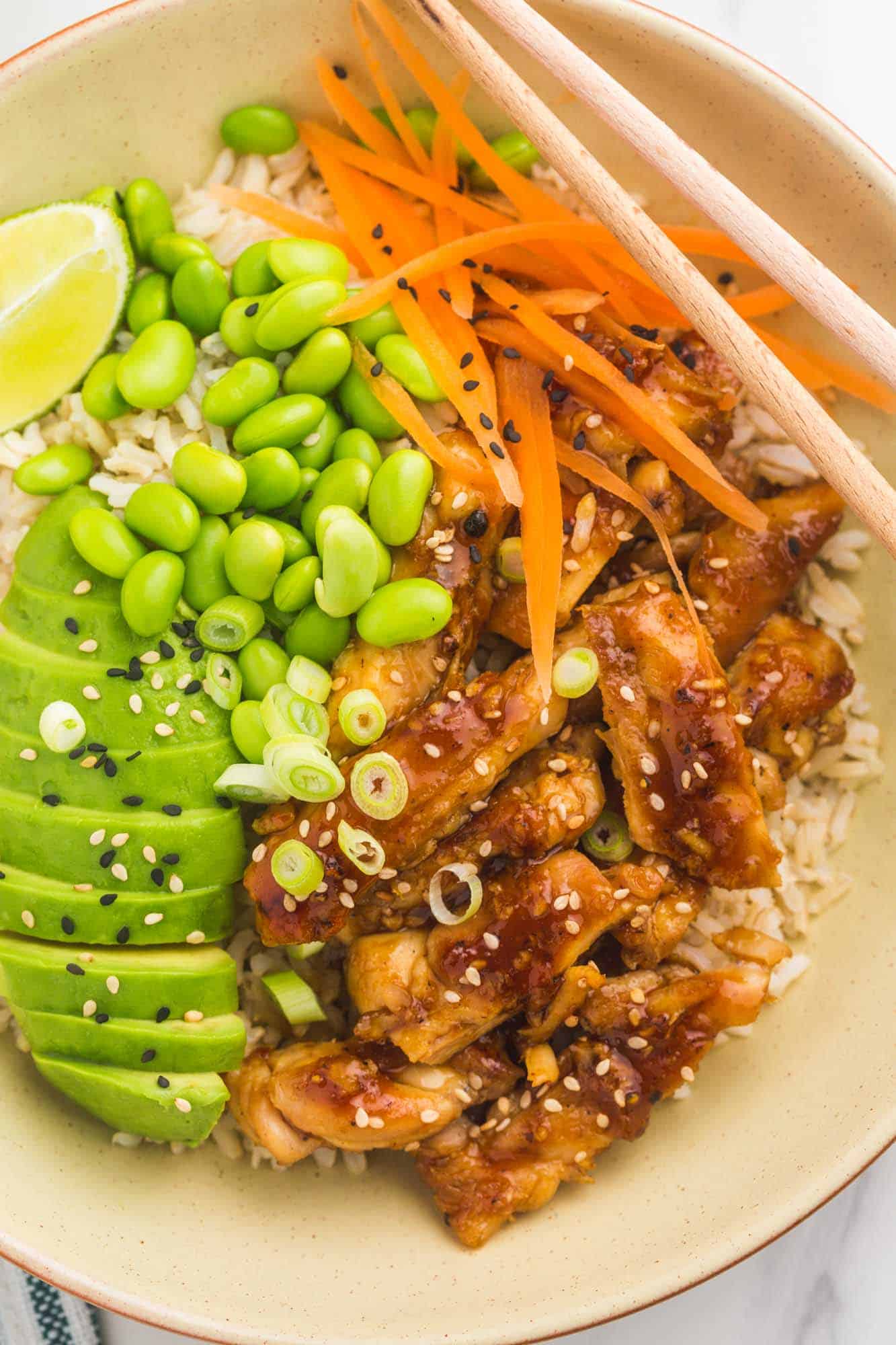 View from above of a teriyaki chicken bowl with avocado, edamame, carrots and rice.