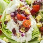 wedge salad topped with blue cheese dressing, red onion, bacon, and cherry tomatoes.