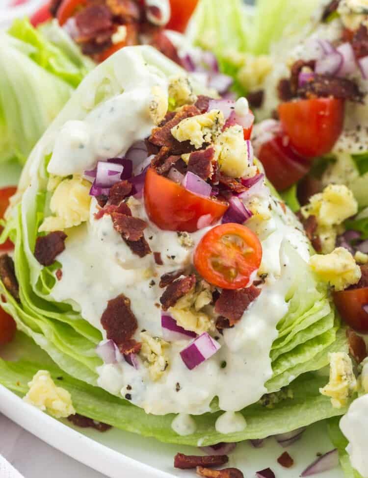 wedge salad topped with blue cheese dressing, red onion, bacon, and cherry tomatoes.