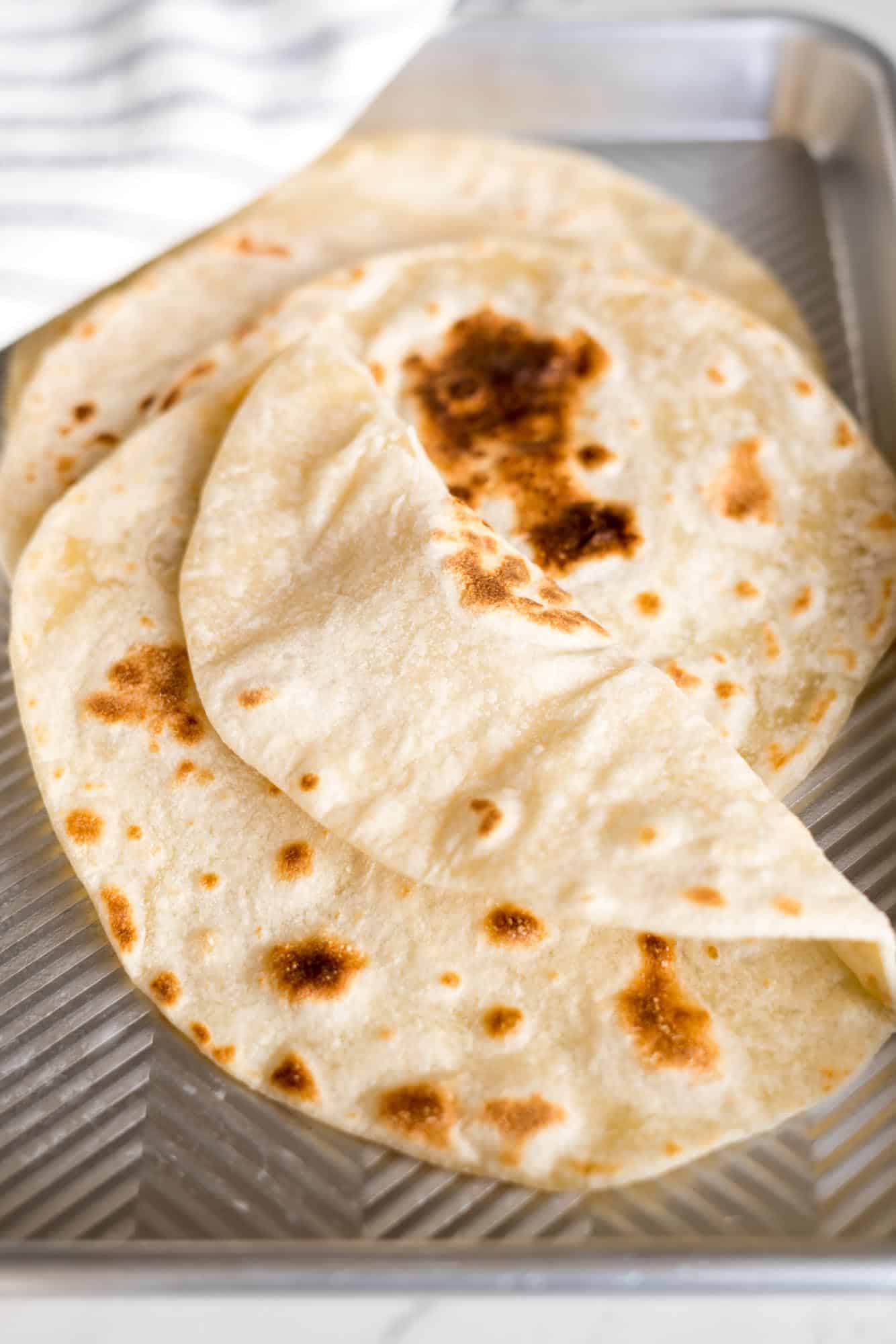 Yogurt flatbreads placed on an aluminum tray, with the front flatbread folded to show that it's pliable. 