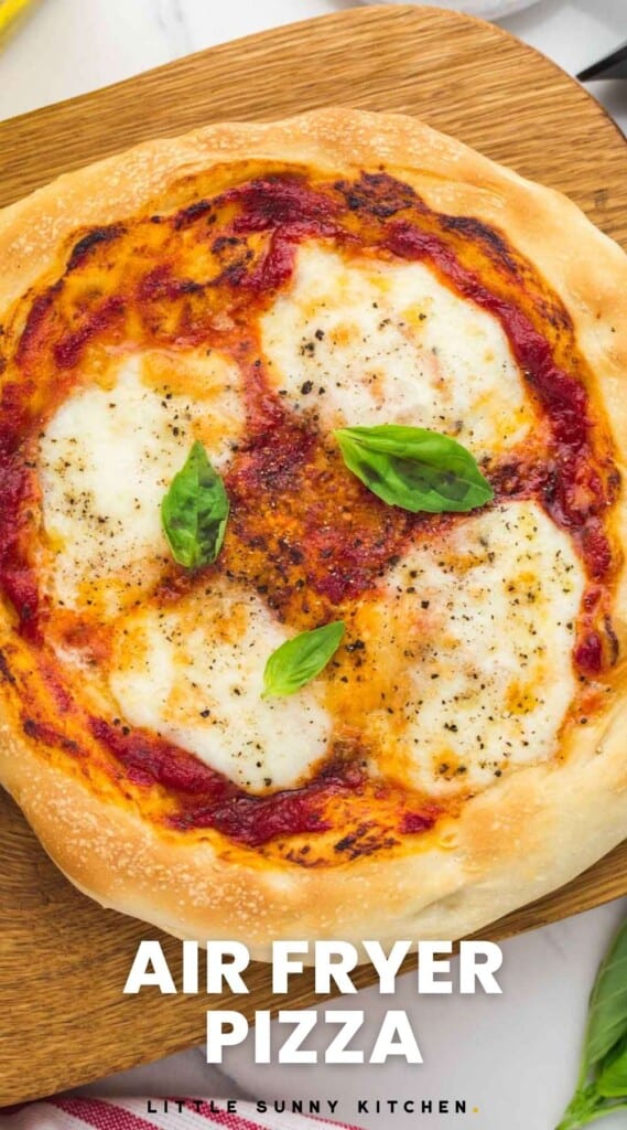 Overhead small pizza placed on a wooden cutting board, topped with mozzarella and basil leaves, and overlay text that says "air fryer pizza"