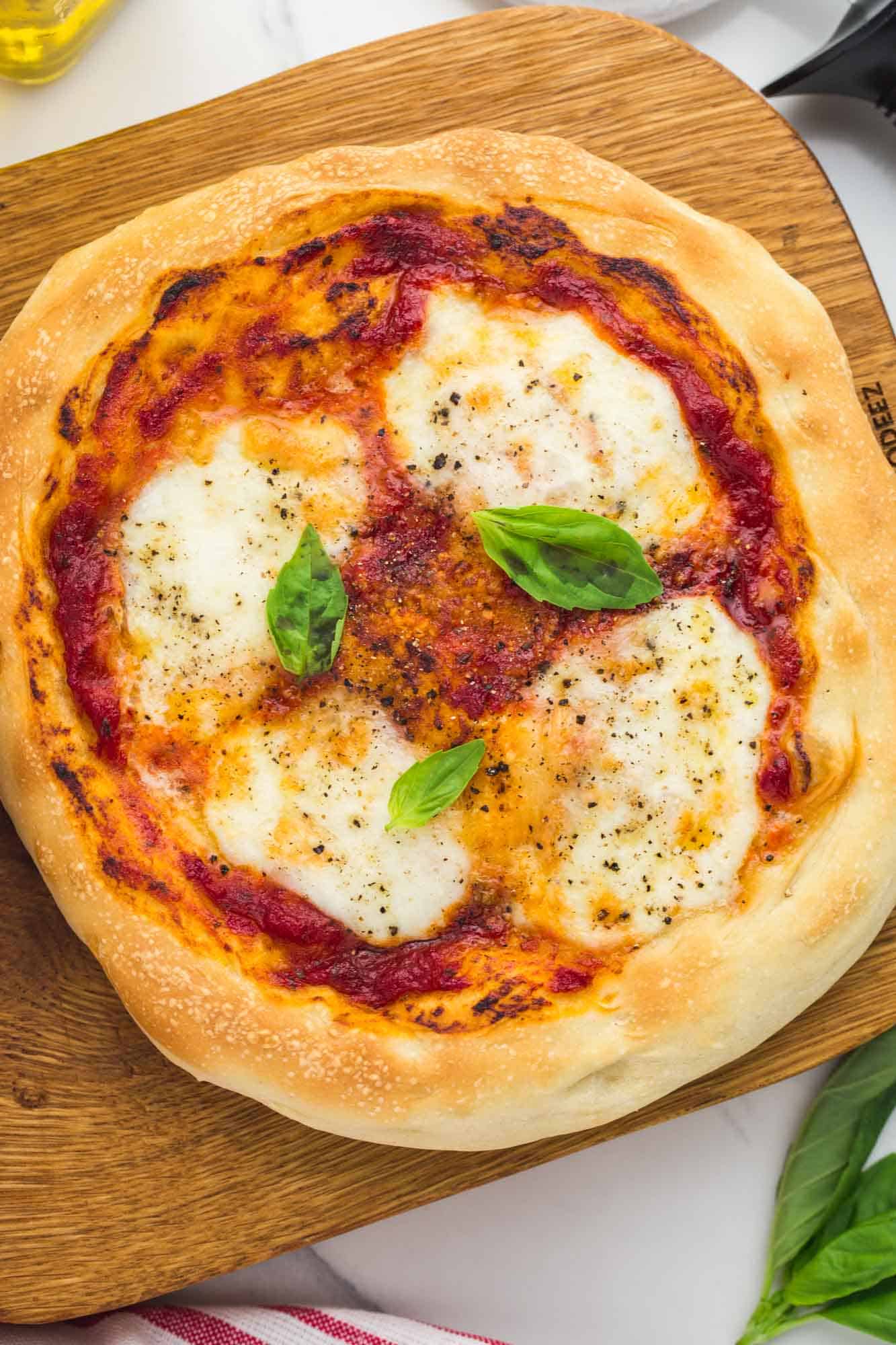 Overhead small pizza placed on a wooden cutting board, topped with mozzarella and basil leaves