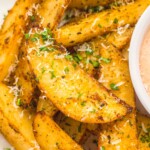 closeup view of crispy baked potato wedges garnished with parmesan and parsley