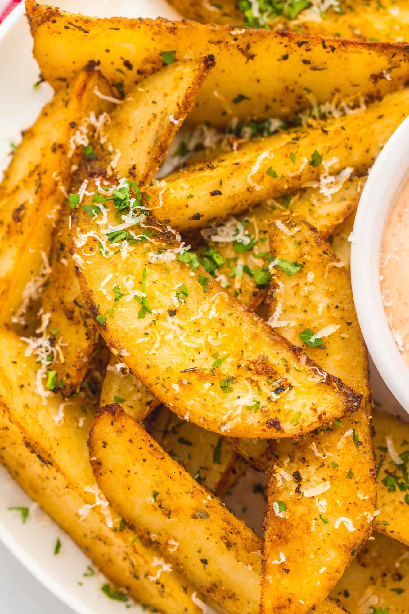 closeup view of crispy baked potato wedges garnished with parmesan and parsley