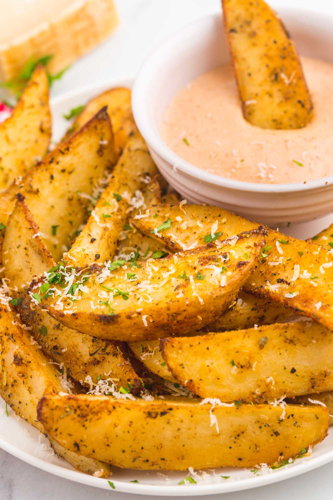 a plate of potato wedges with one being dipped into a cup of fry sauce