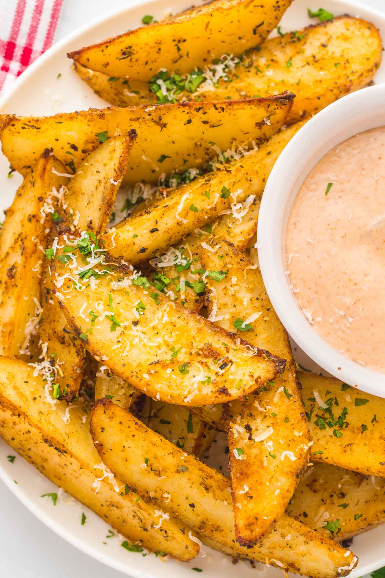 cropped image showing half of a plate of baked russet wedges and a cup of fry sauce in the center.
