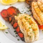 Broiled and seasoned lobster tails served on a plate with lemon wedges
