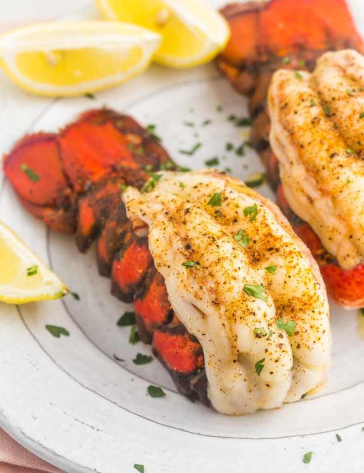 Broiled and seasoned lobster tails served on a plate with lemon wedges