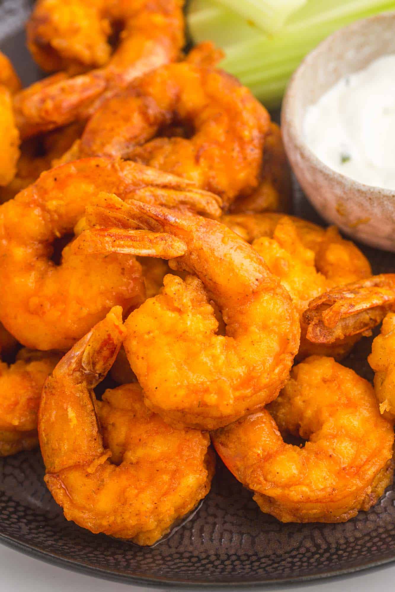 fried buffalo shrimp on a black plate next to a side of blue cheese and celery 