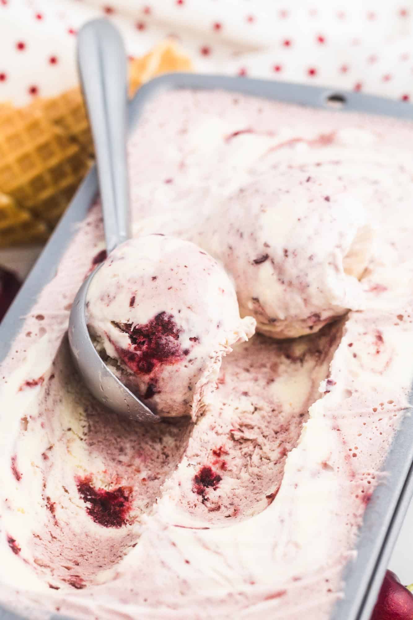 Scooping ice cream from a loaf pan, showing the texture of the cherry and vanilla ice cream