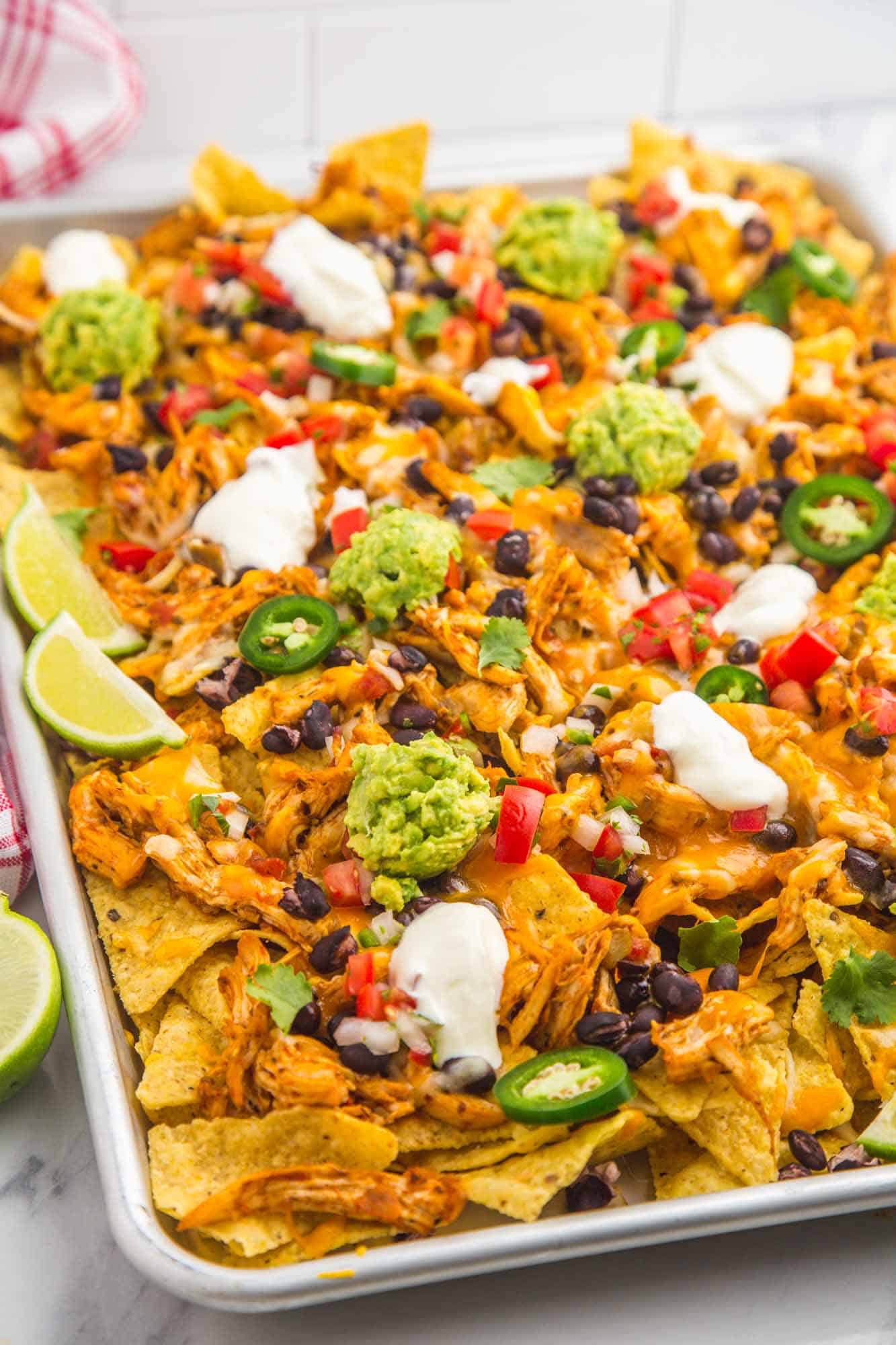 a sheet tray of chicken nachos, loaded with toppings.
