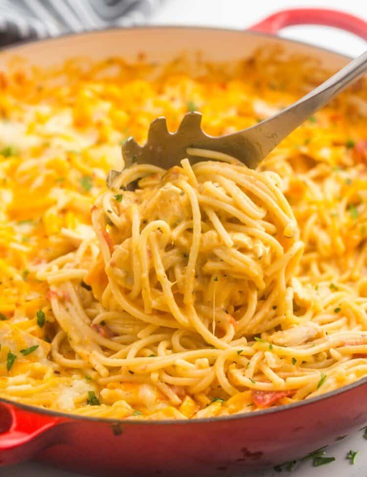 chicken spaghetti in a large red skillet, being served with a pasta spoon