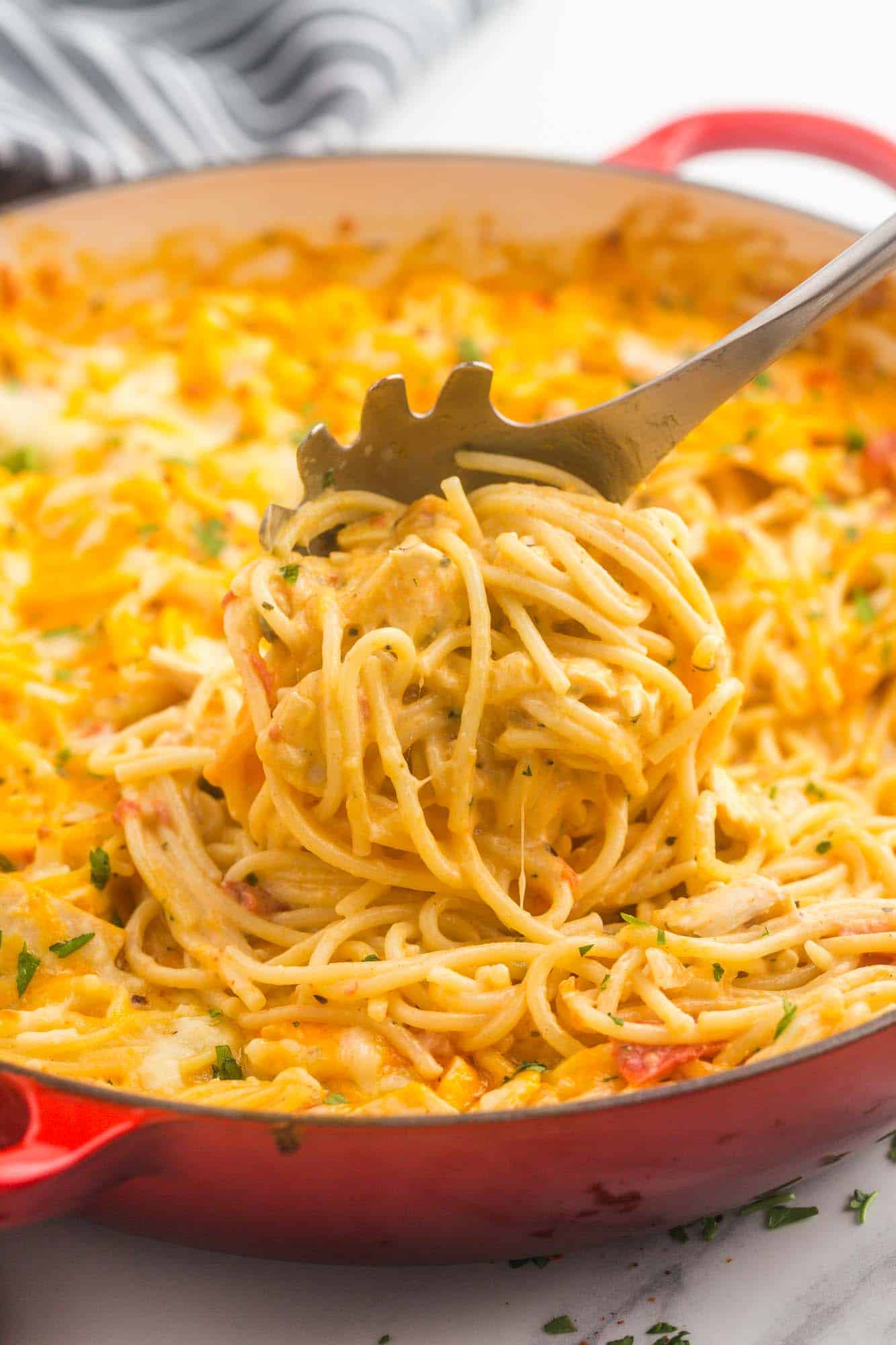 chicken spaghetti in a large red skillet, being served with a pasta spoon