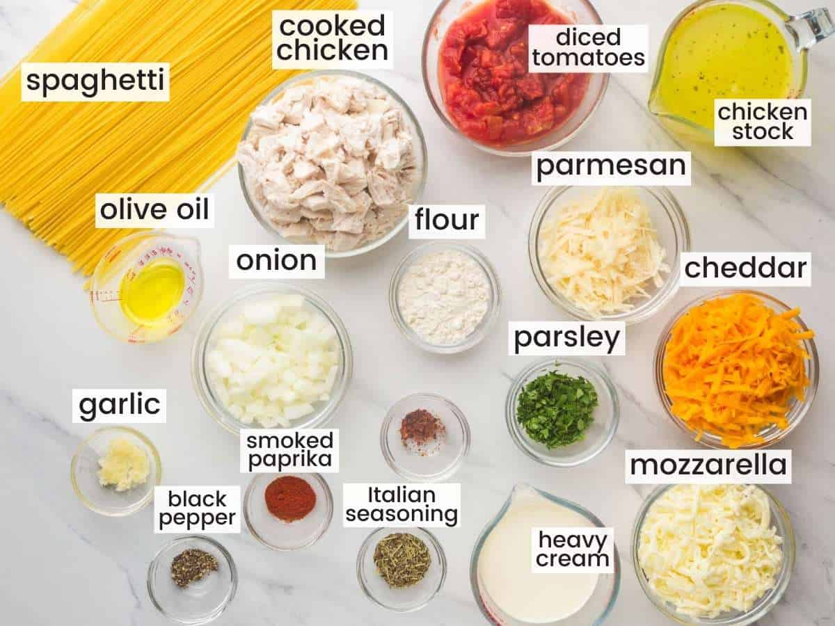 The ingredients for chicken spaghetti, all measured into small glass bowls, on a counter next to a pile of dry spaghetti pasta. 