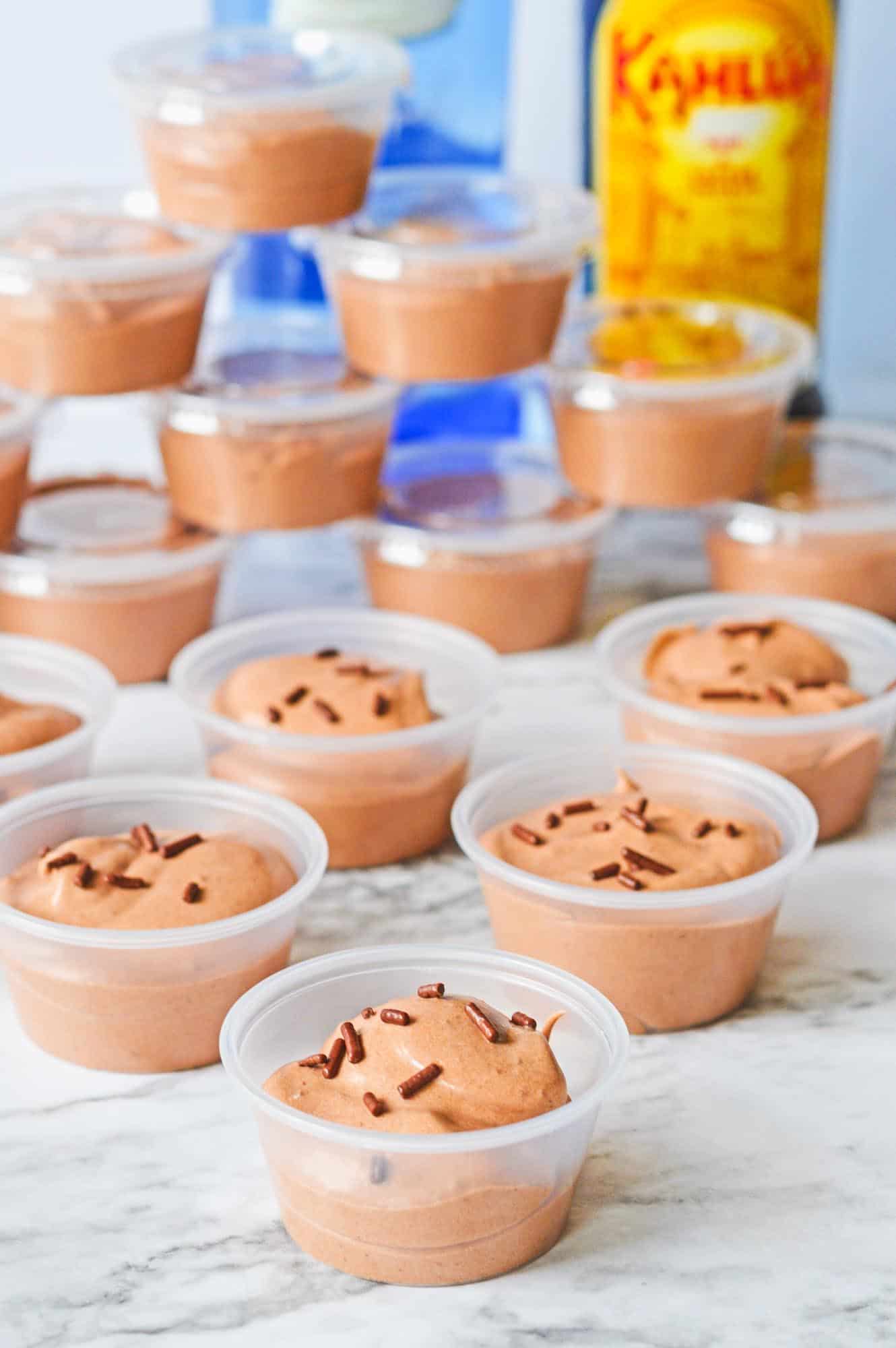 chocolate pudding shots in small plastic containers lined up on the counter. A bottle of kahlua is in the background