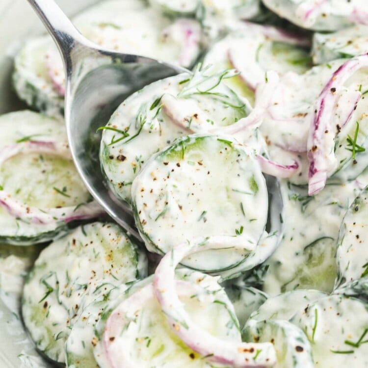 a bowl of creamy cucumber salad with dill. A spoon is serving from it.