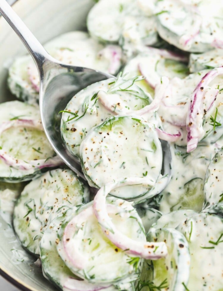 a bowl of creamy cucumber salad with dill. A spoon is serving from it.