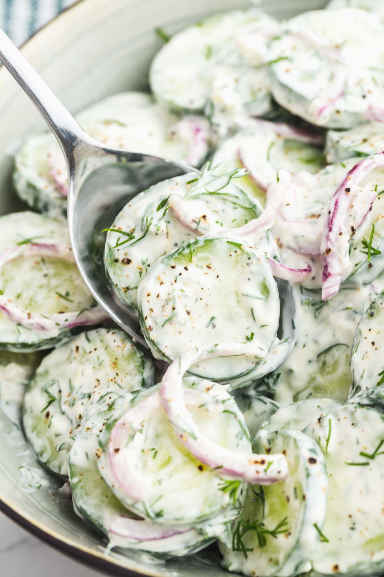 a bowl of creamy cucumber salad with dill. A spoon is serving from it.