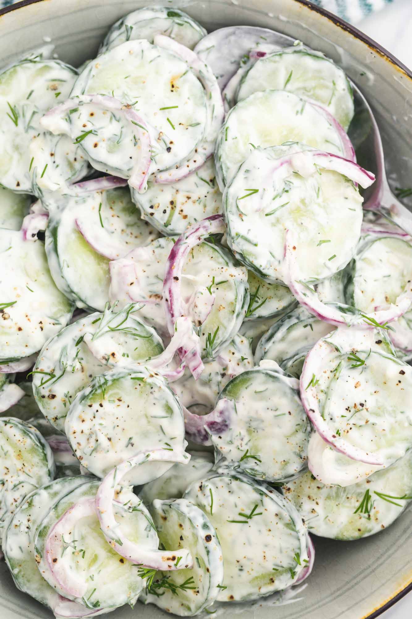 A silver mixing bowl filled with creamy salad of sliced cucumbers and onion