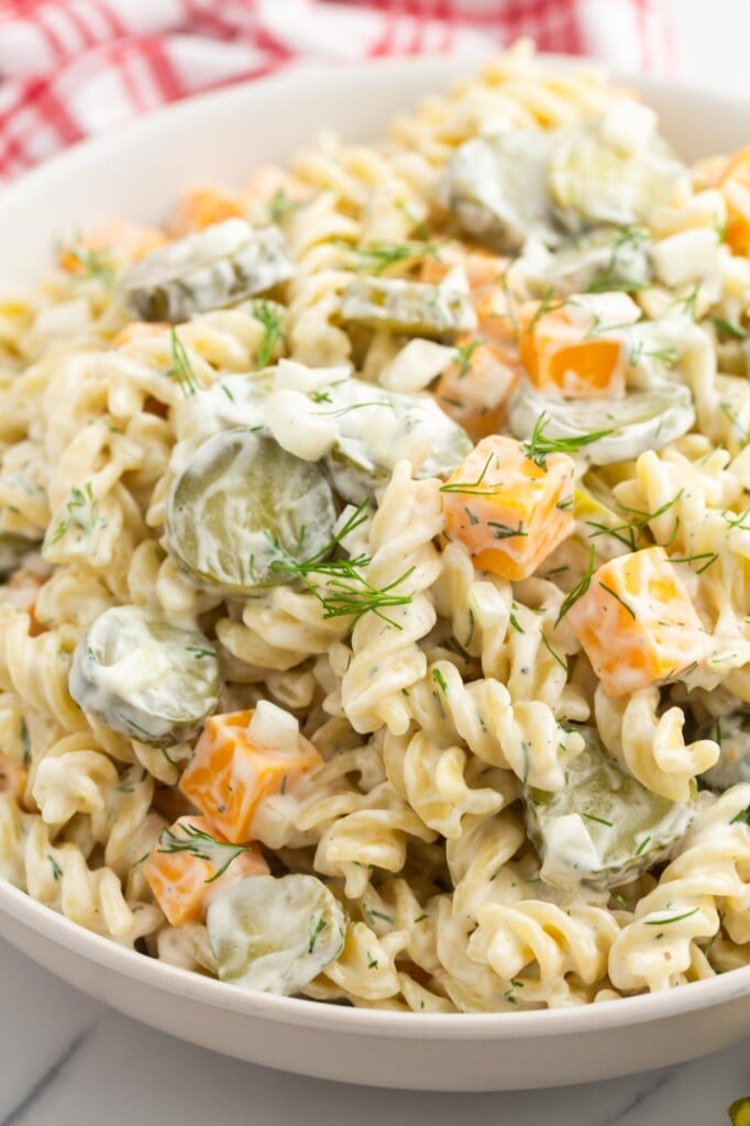 a bowl of dill pickle pasta salad with rotini, cubed cheese, and sliced pickles, garnished with dill.