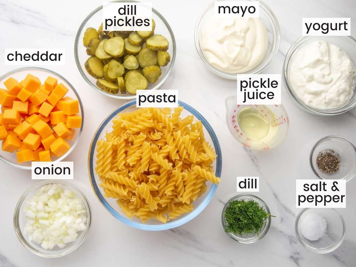 The ingredients needed to make dill pickle pasta salad with cheese, all measured into separate glass bowls on a countertop.