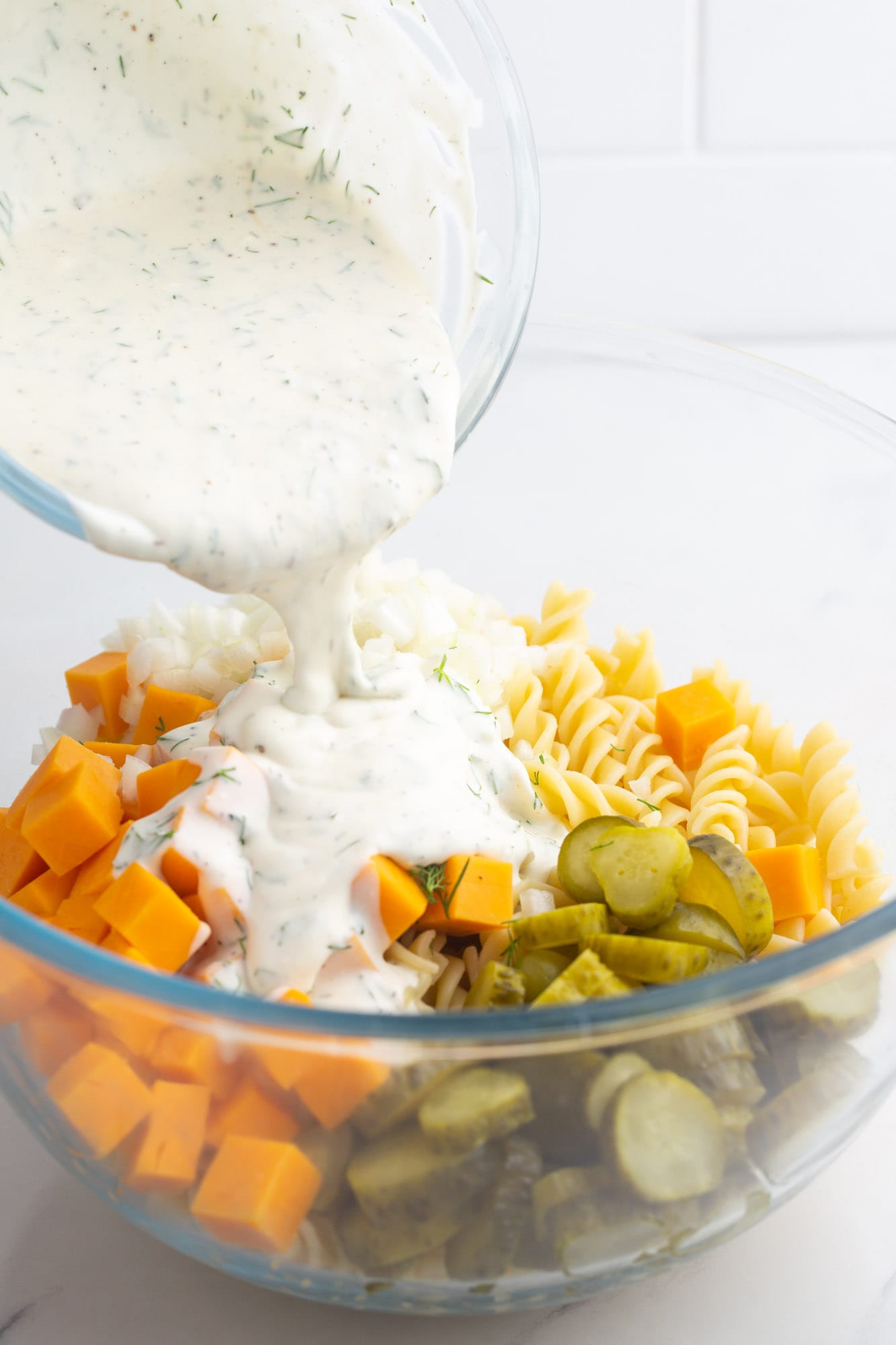 Pouring creamy dill dressing over the ingredients for pickle pasta salad