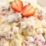 a white bowl filled with creamy fruit salad with whipped cream and marshmallows, topped with strawberry garnish