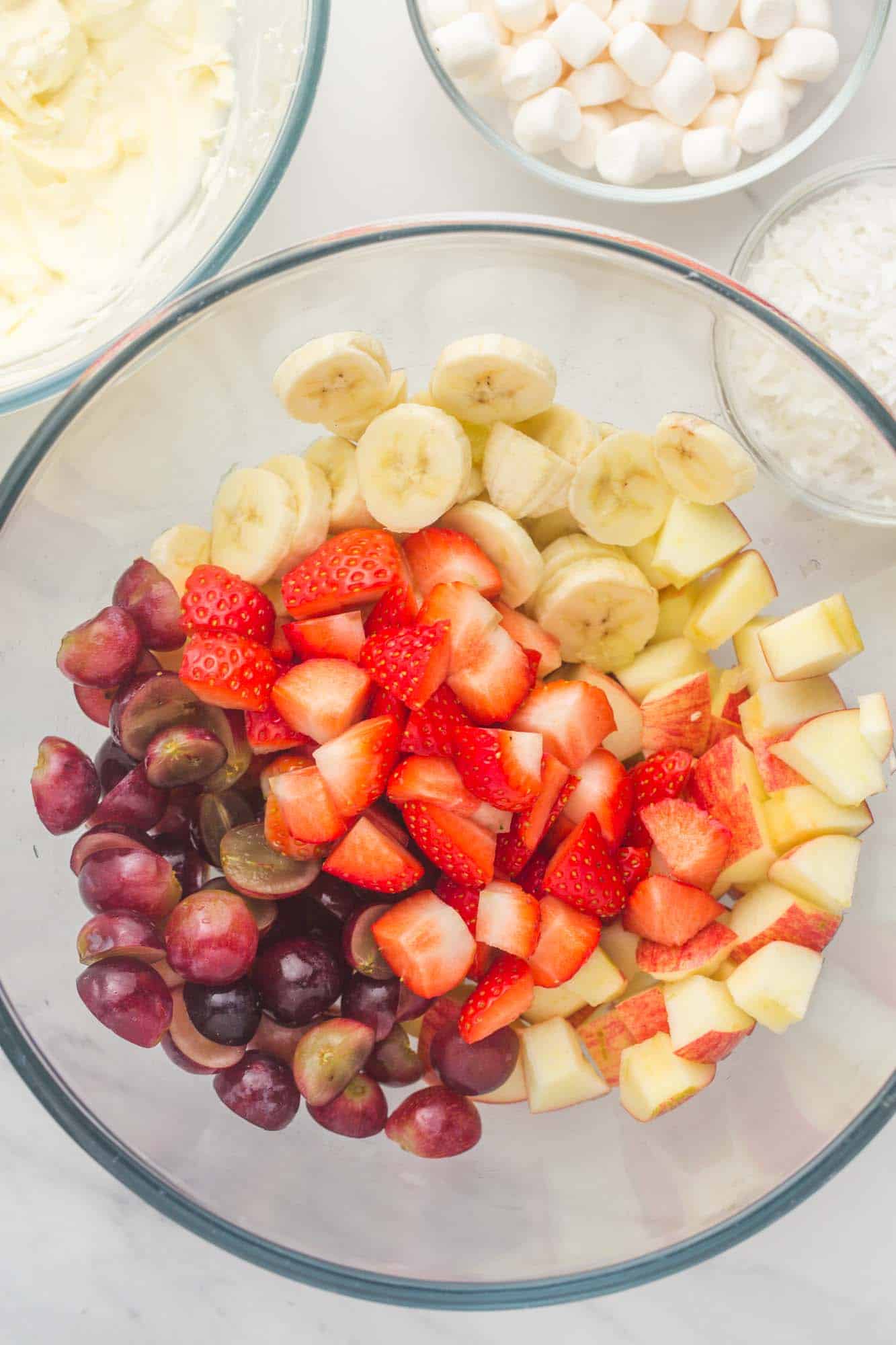 a clear bowl filled with mixed cut fruit including strawberries, grapes, and bananas