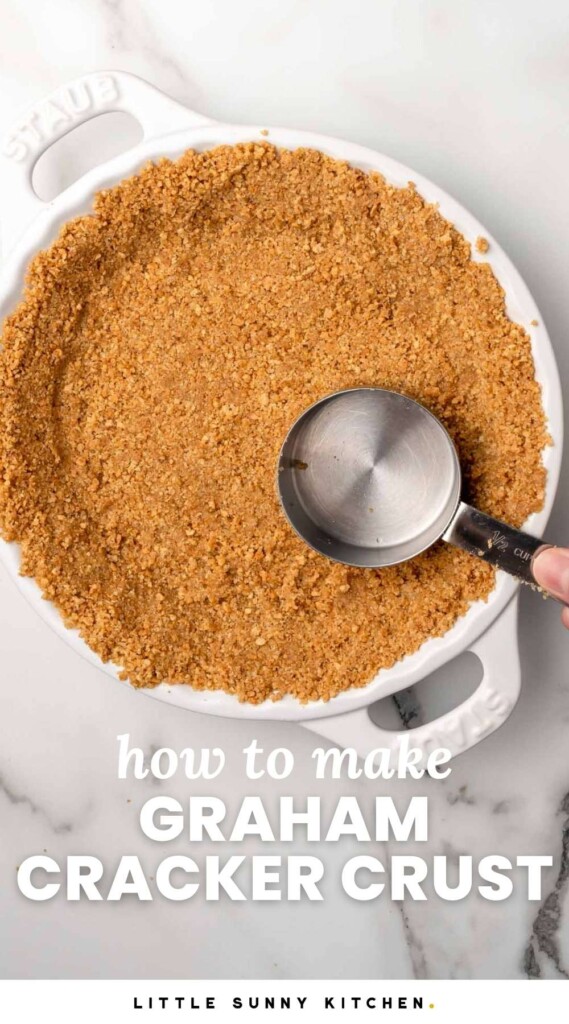 graham cracker crust being pressed into a white ceramic pie plate with a measuring cup