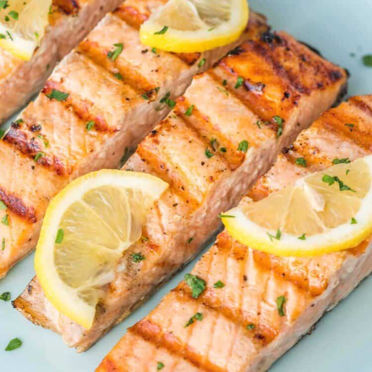 Salmon filets with pronounced grill marks, topped with lemon slices, and resting on a light blue plate.