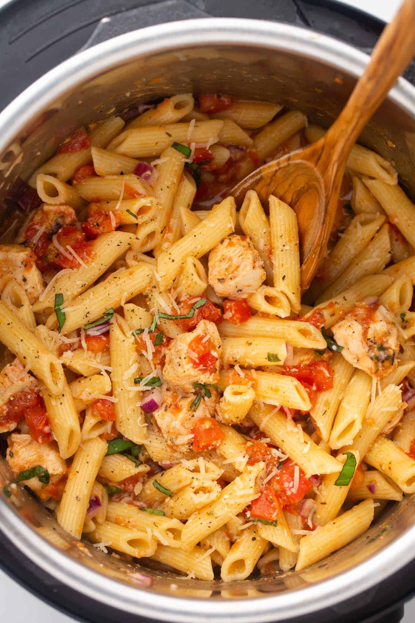 Overhead shot of bruschetta chicken pasta in the instant pot with a wooden spoon
