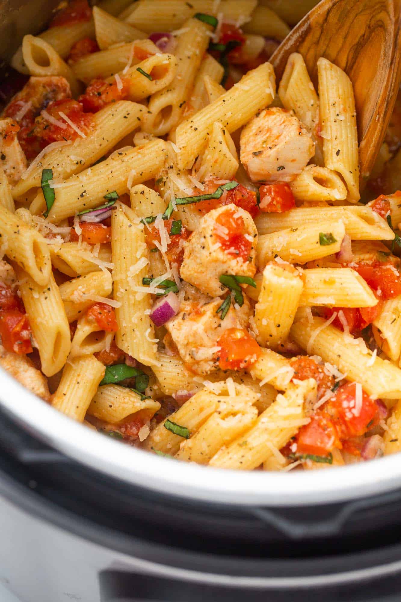 Close up shot of bruschetta chicken pasta in the instant pot with a wooden spoon