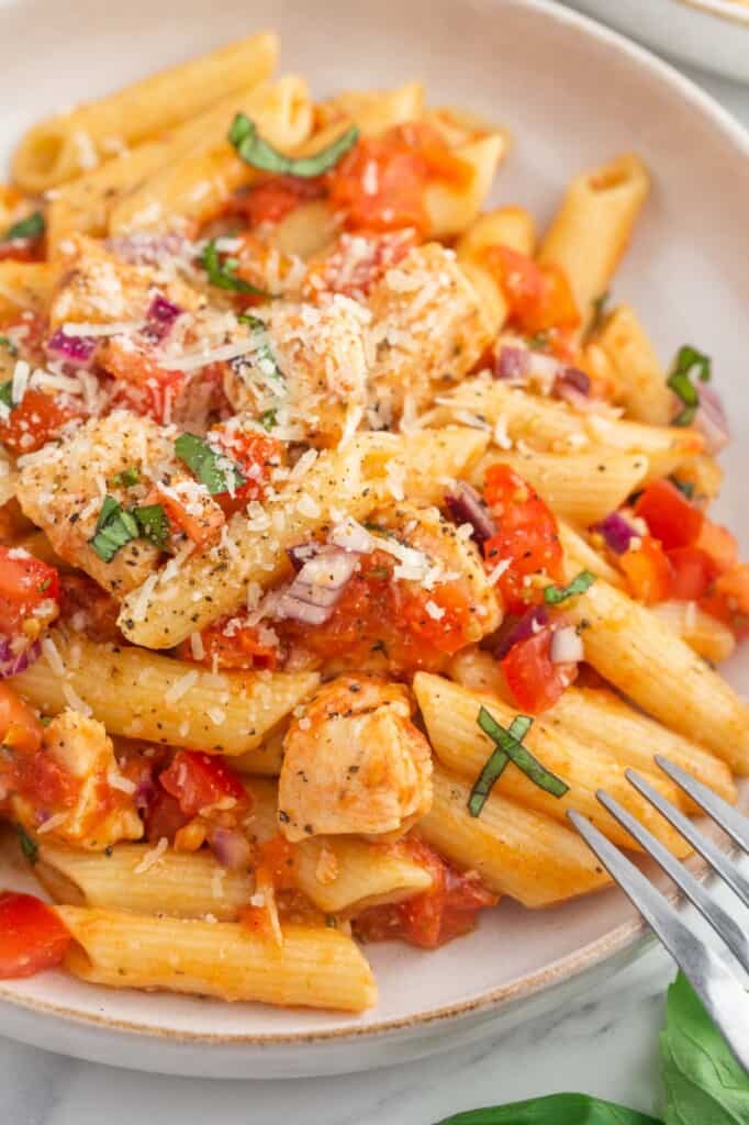 Bruschetta chicken pasta served in a pasta bowl, with extra parmesan cheese and a fork on the side.