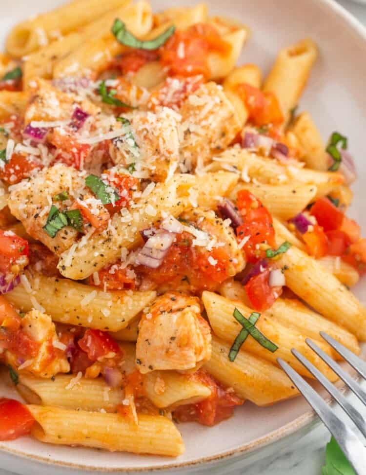 Bruschetta chicken pasta served in a pasta bowl, with extra parmesan cheese and a fork on the side.